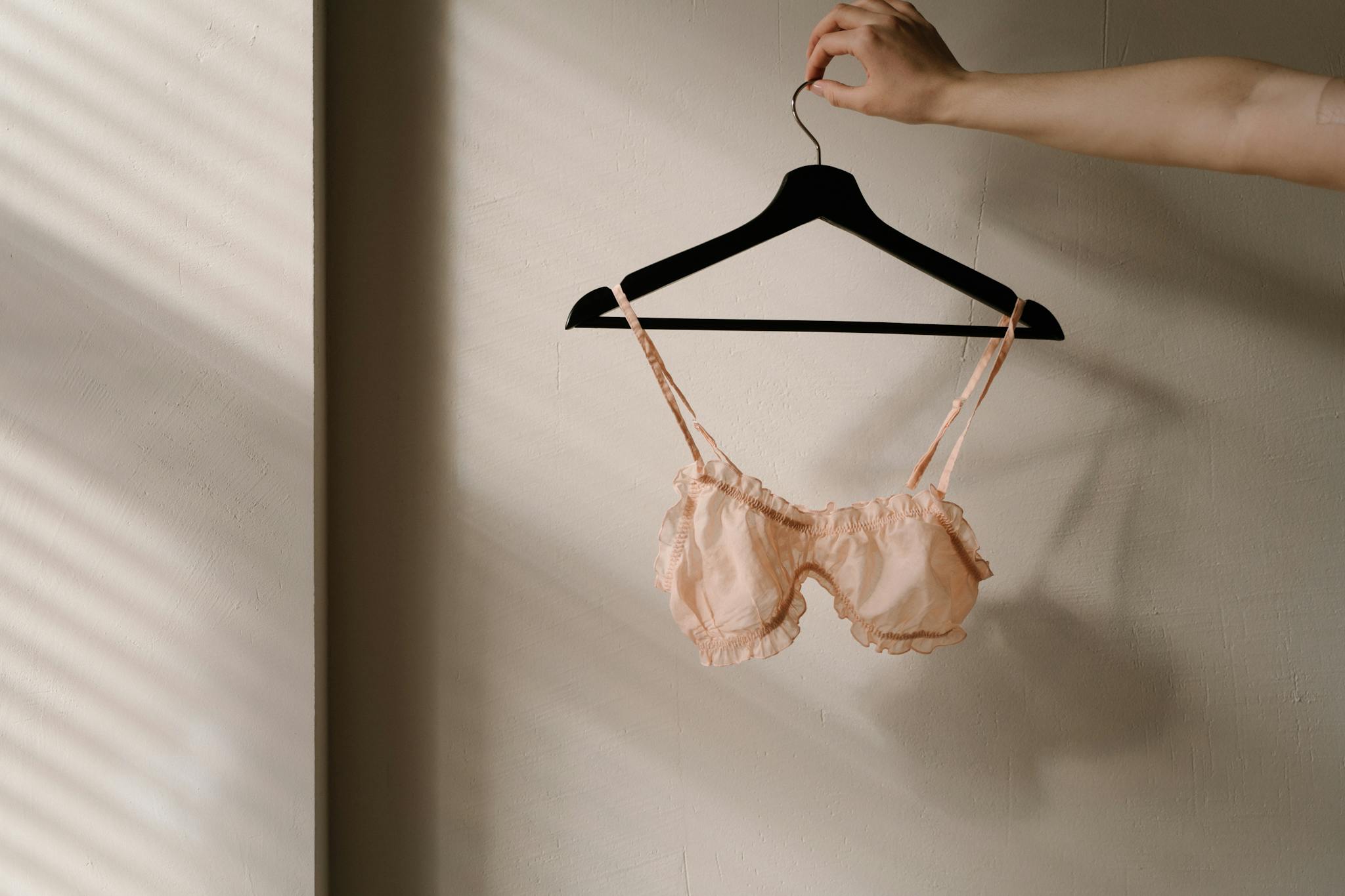 A delicate pink bra on a hanger, captured in a minimalistic indoor setting with soft lighting.